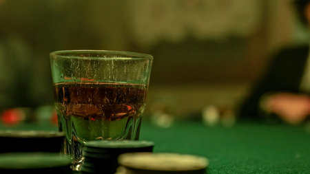 A man is pouring whiskey into a glass placed on a poker table covered in green felt. Surrounding the...