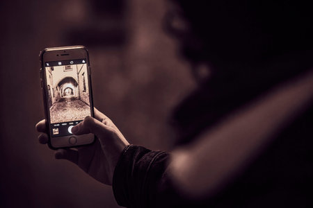 A photo of a young man taking a picture in an alley at night using his smartphone, capturing the...