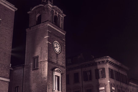A photo showing the architectural details of buildings in Ferrara's city center at night. The...