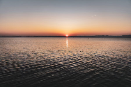 Beautiful sunset over the stunning Garda Lake in Italy, with the sun reflecting on the calm water...