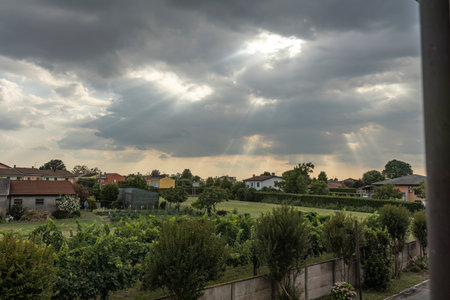 Sun rays breaking through clouds, illuminating a serene countryside village below.の写真素材