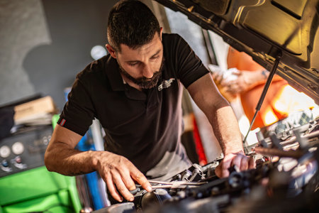 Milan, Italy 9 April 2024: Mechanic's hands delve into car engine under the hood, symbolizing repair and maintenance.のeditorial素材
