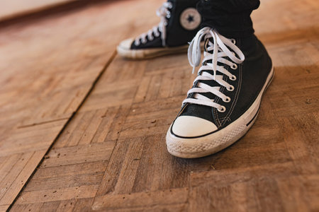 Milan, Italy 12 June 2024: A close-up shot of a person wearing black Converse sneakers with white laces, standing on an old wooden floor with visible cracks and wear. The image highlights the casual, vintage feel of the scene.のeditorial素材