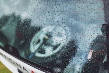 Close-up of rain drops on a rally car rear window with reflections of the interior and outsideの写真素材