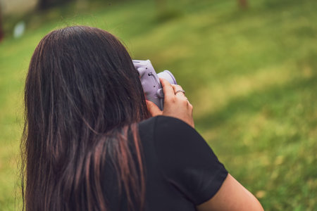 Back view of a woman using an instant camera to take a photo in a grassy areaの写真素材