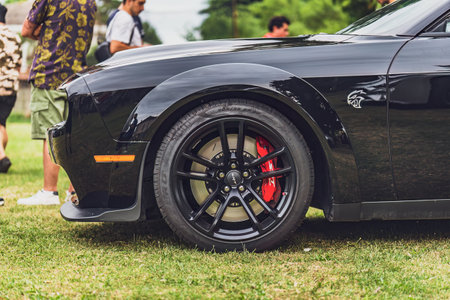 Gavello, Italy 23 June 2024: Close-up view of a black Dodge Challenger's wheel featuring red brake calipers, parked on grassのeditorial素材