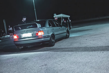 Adria, Italy 30 July 2024: Gray BMW E36 with custom spoiler and wheels parked at a gas station at nightのeditorial素材