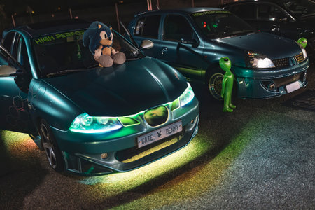Adria, Italy 30 July 2024: A blue modified car with a Sonic plush toy on the hood and neon lights, parked next to another modified car at night.のeditorial素材