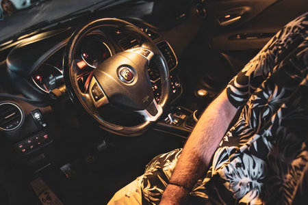 Adria, Italy 30 July 2024: View of a car interior featuring the steering wheel and driver in a patterned shirt, illuminated dashboardのeditorial素材
