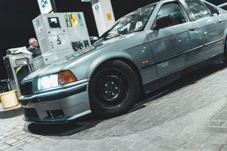 Adria, Italy 30 July 2024: Gray BMW E36 with custom spoiler and wheels parked at a gas station at nightのeditorial素材