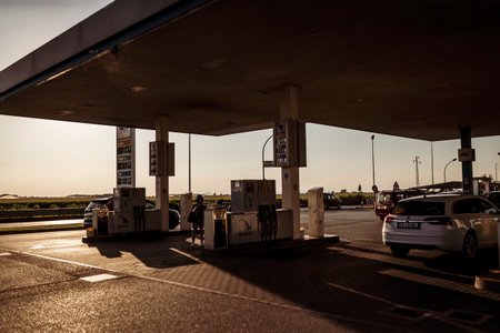 Adria, Italy 30 July 2024: Multiple cars parked at a gas station during sunset with long shadows.のeditorial素材