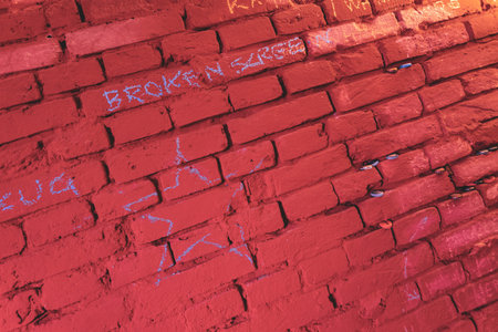 Closeup of a red brick wall with chalk graffiti and carvings etched into the surface.