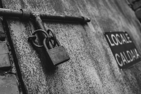 A closeup of a rusty padlock on a metal bar, highlighting textures of decay and aged materials in black and white.の写真素材