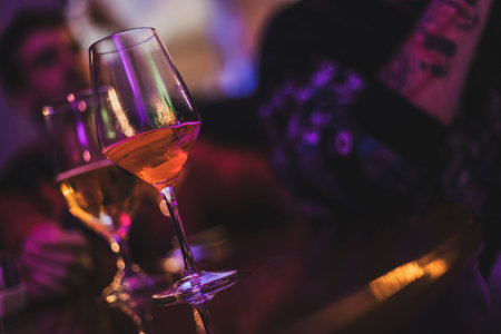 Wine glasses filled with beverages sit on a bar during an evening gathering, creating a vibrant and social atmosphereの写真素材
