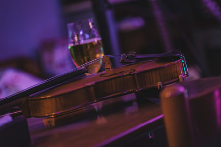 Violin lies on a table next to a glass of beer, creating a cozy and musical atmosphere in a dimly lit pubの写真素材