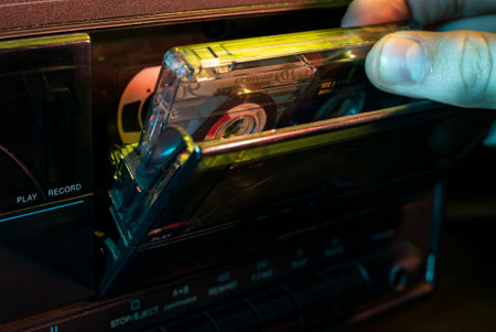 Hand inserting audio cassette tape into vintage stereo player with play and record buttons in neon lightの写真素材