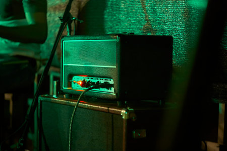 Guitar amplifier glowing under green stage lights during a live musical performance