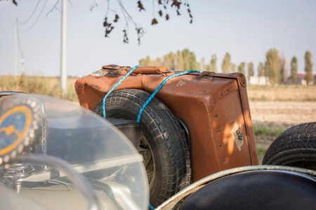 Brown vintage suitcase and spare tire are fastened with rope to the sidecar of a motorcycle parked outdoorsの写真素材