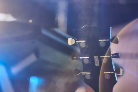 Close-up of electric guitar headstock with tuning pegs, bathed in blue and purple stage lights, creating a moody atmosphereの写真素材