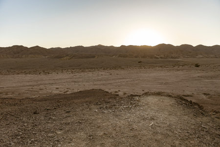 Rocky terrain leading to vast desert landscape with mountains in the background and setting sunの写真素材