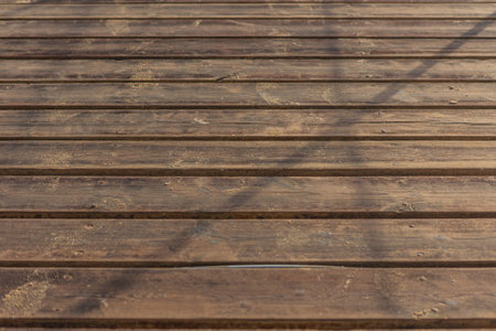 Close-up view of a weathered wooden boardwalk with traces of sand, creating a textured background...