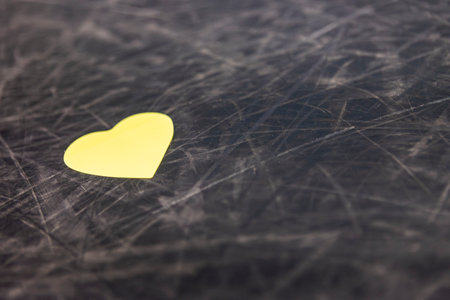 Yellow paper heart shape lying on scratched black surface, representing concepts like love, affection, and valentine's dayの写真素材