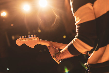 Close-up of a guitarist's hands playing electric guitar on a brightly lit stage, creating a captivating musical atmosphereの写真素材