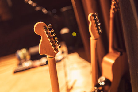 Electric and acoustic guitar necks stand on a stage, bathed in the warm glow of stage lights, ready for a music performanceの写真素材