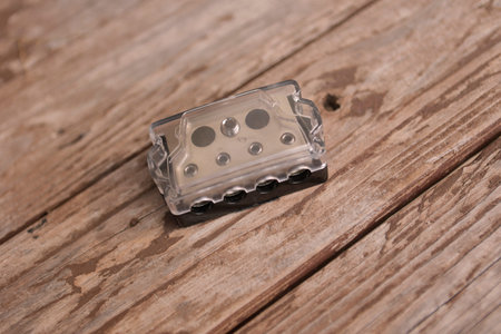 Transparent automotive fuse block with brass connectors lying on a weathered wooden table, ensuring...