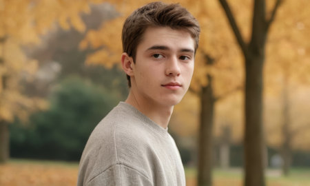 Portrait of a young man posing in a serene park, surrounded by vibrant autumn foliage in stunning shades of gold, yellow, and orangeの素材