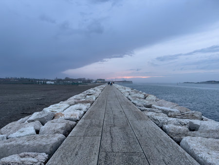 Tourists strolling along the murazzi, a picturesque stone seawall in sottomarina, italy, enjoying the tranquil beauty of duskの写真素材