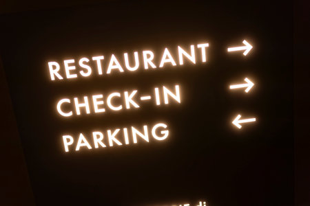 Luminous sign glowing brightly in the dark, guiding travelers with clear directions for restaurant access, check-in, and parking facilitiesの写真素材