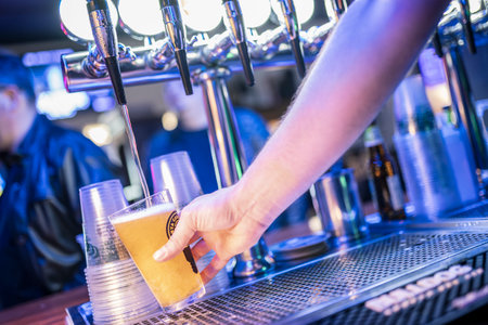 Rome, Italy 4 May 2025: bartender serving a refreshing pint of beer from a tap in a bustling bar settingの写真素材
