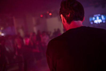 Rome, Italy 4 May 2025: dj performing live electronic music with people dancing in nightclub, illuminated by red and purple lightsの写真素材