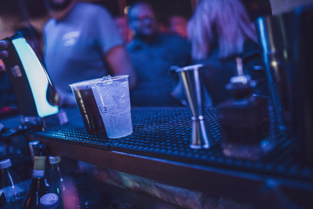 Rome, Italy 4 May 2025: plastic glasses with alcoholic beverages and ice cubes standing on bar counter in nightclub, bartender preparing cocktailsの写真素材
