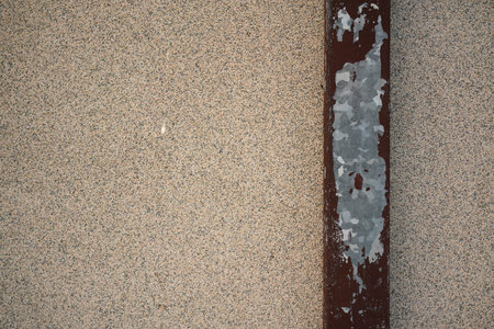Close up view of a rusty metal beam with peeling silver paint against a textured, granulated wall,...