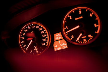 close up of an illuminated car dashboard displaying speed, rpm, temperature, and other information in a warm red glowの写真素材