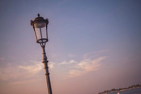 ornate street lamp silhouetted against a beautiful sunset sky in chioggia, italy, creating a...