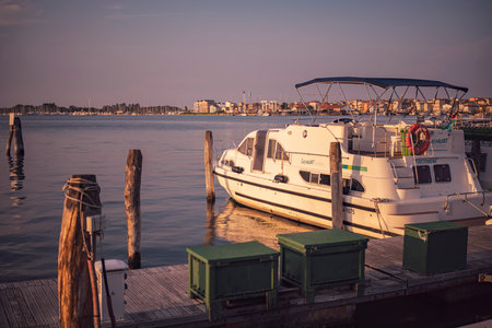 Chioggia, Italy 21 June 2025, scenic view of a white motorboat moored at a wooden pier in Sottomarina, Chioggia, Italy, during a golden sunsetの写真素材