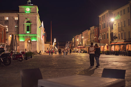 Chioggia, Italy 21 June 2025, tourists walking along Corso del Popolo in Chioggia, Italy, at night, passing by the town hall and restaurantsの写真素材