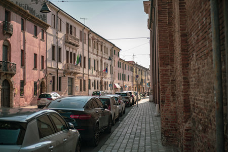 Rovigo, Italy 21 June 2025, parked cars lining a narrow street in Rovigo, Italy, with colorful buildings and brick walls on a sunny summer dayの写真素材