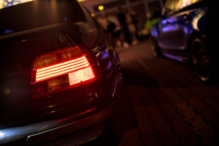 Red rear car lights illuminating a dark parking lot at night create a dramatic and mysterious...
