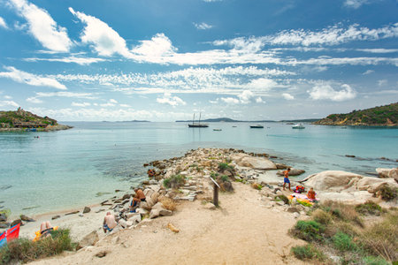 Tourists relaxing on the beautiful Punta Molentis beach in Villasimius, Sardinia, Italy, with turquoise water and boats in the backgroundの写真素材
