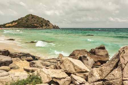 Gentle waves washing over rocks on the beach of monte turnu, italy, with a cloudy sky and tourists enjoying the seaの写真素材