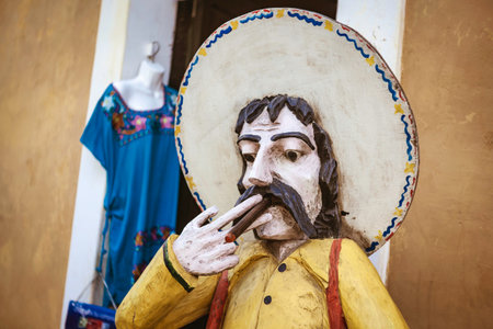 Traditional wooden statue of a mexican man wearing sombrero and smoking a cigar, representing local culture and craftsmanship in valladolid, mexicoの写真素材