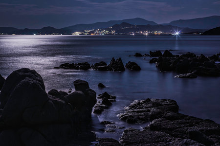Tranquil night scene at Capo Ferrato beach in Sardinia, Italy, with moonlight reflecting on the calm sea and illuminating the coastlineの写真素材