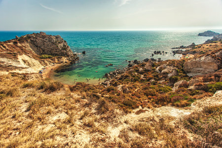 Tourists swimming in the crystal-clear turquoise waters of Cala Paradiso beach in Sicily, Italy, surrounded by rocky cliffs and vegetationの写真素材