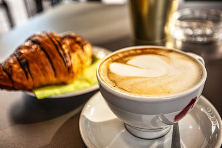 Creamy cappuccino with latte art heart shape served with a chocolate croissant, creating the perfect...
