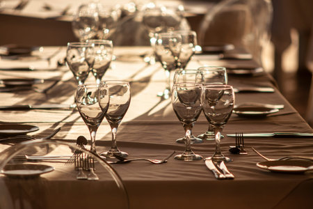 Empty wine glasses and cutlery are placed on a long table in a restaurant, creating an elegant...