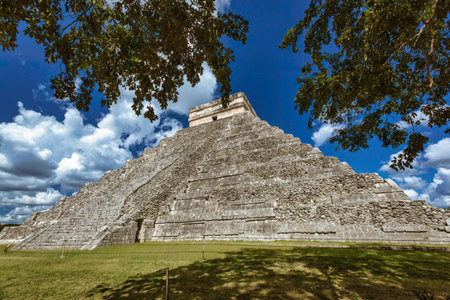 Kukulkan temple, an ancient Mayan pyramid, stands tall against a vibrant blue sky dotted with fluffy...